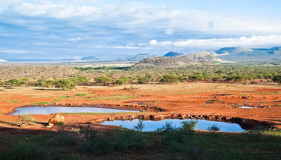 The waterhole below Kilaguni inside Tsavo West National Park, with the red volcanic earth and hills beyond